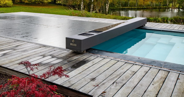 Image montrant une piscine extérieure équipée d'une couverture automatique moderne sur un terrassement en bois, située dans un cadre naturel verdoyant