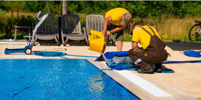 Photo au format paysage montrant deux techniciens au bord d'une piscine en train d'en réaliser la maintenance afin de la remettre en service après l'hiver. Cette photo illustre l'estivage d'une piscine.