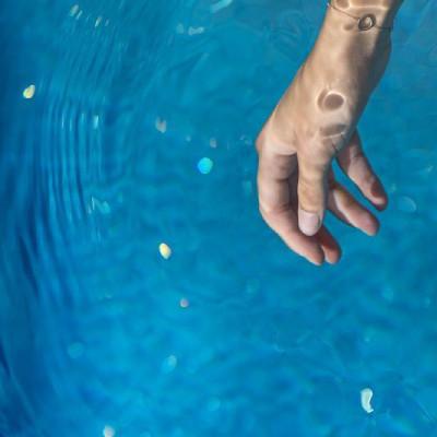 Photo montrant des mains au dessus de l'eau d'une piscine. Une main plonge dans l'eau une languette d'analyse, l'autre tient un flacon.